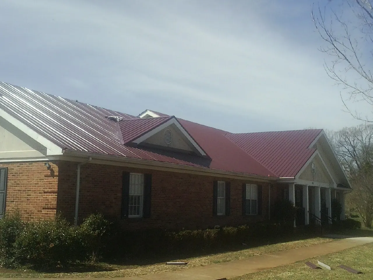 Red metal roof with gabled entries on a long brick building, from a Hail Damage Roof Repair job in Mascot